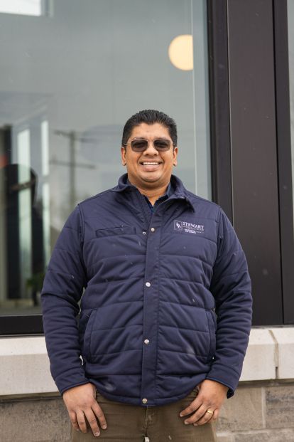 Image of a man standing in front of a window with outdoor wear and sunglasses on