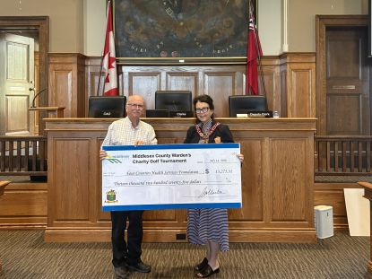 Two people stand holding a large cheque. 