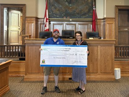 Two people stand holding a large cheque. 
