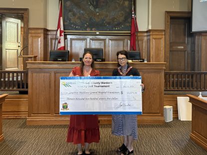 Two people stand holding a large cheque. 